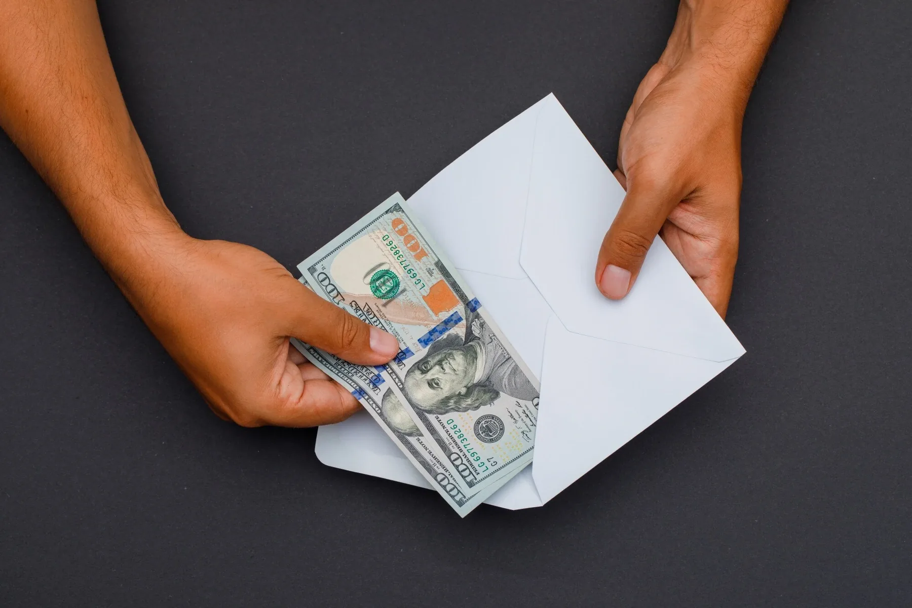 Hands placing hundred dollar bills into an envelope