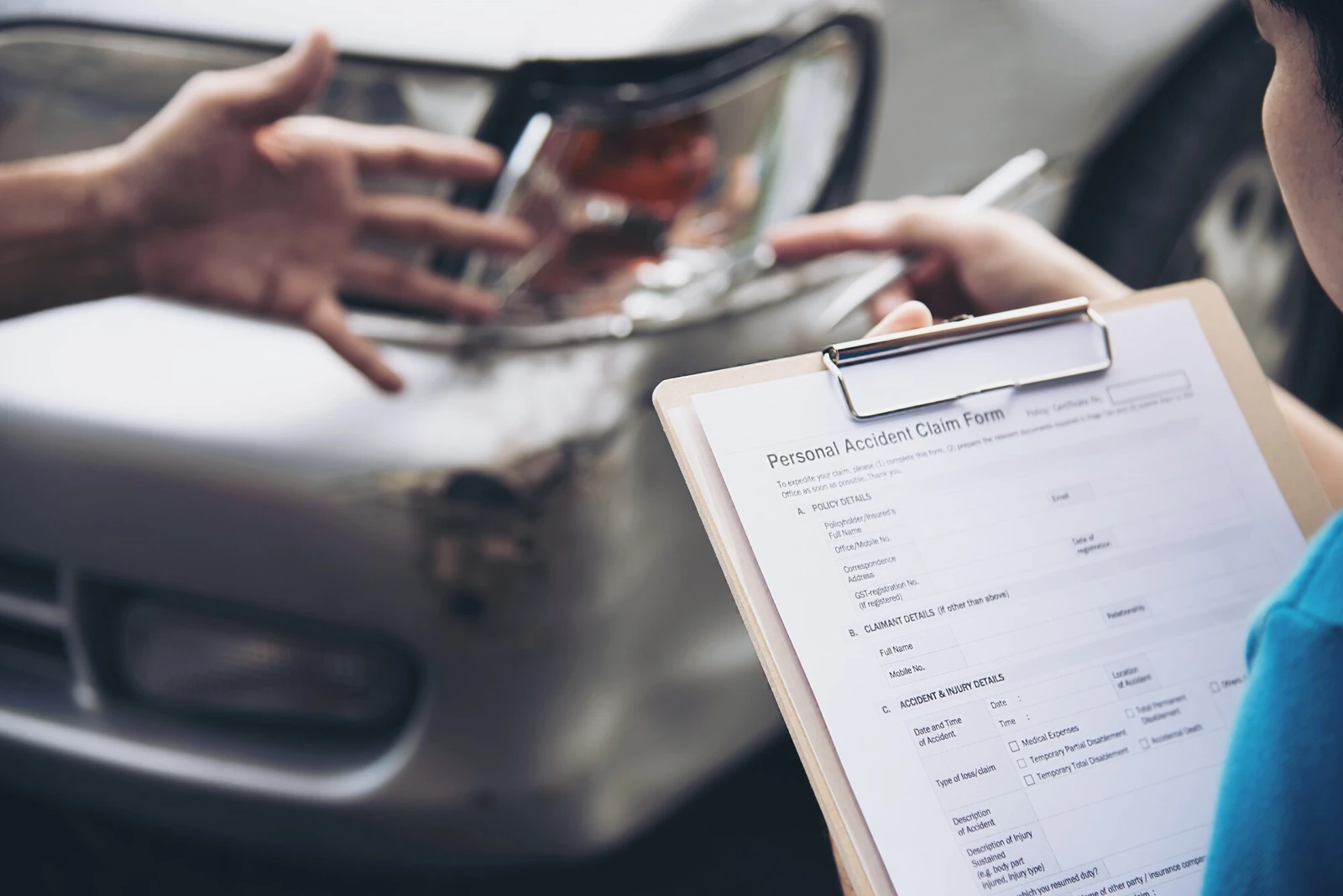 A personal accident claim form held beside a damaged car